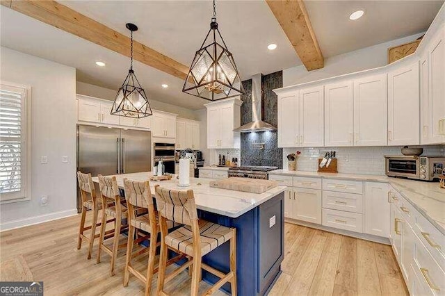 kitchen with a kitchen island with sink, white cabinets, wall chimney range hood, beam ceiling, and a breakfast bar area