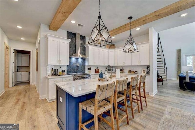 kitchen with wall chimney range hood, stove, a kitchen bar, a center island with sink, and white cabinets