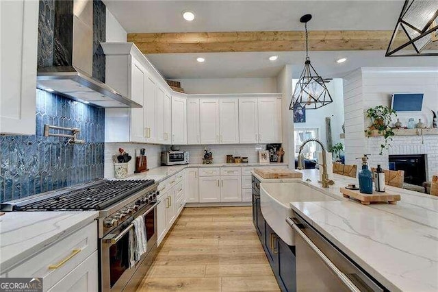 kitchen featuring stainless steel appliances, wall chimney range hood, beam ceiling, decorative light fixtures, and white cabinets