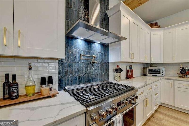 kitchen featuring light stone countertops, backsplash, wall chimney exhaust hood, stainless steel range, and white cabinetry