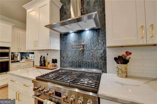 kitchen featuring white cabinets, appliances with stainless steel finishes, light stone counters, and wall chimney range hood