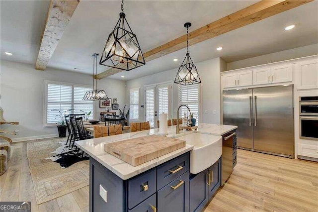 kitchen featuring white cabinetry, sink, stainless steel appliances, an island with sink, and pendant lighting