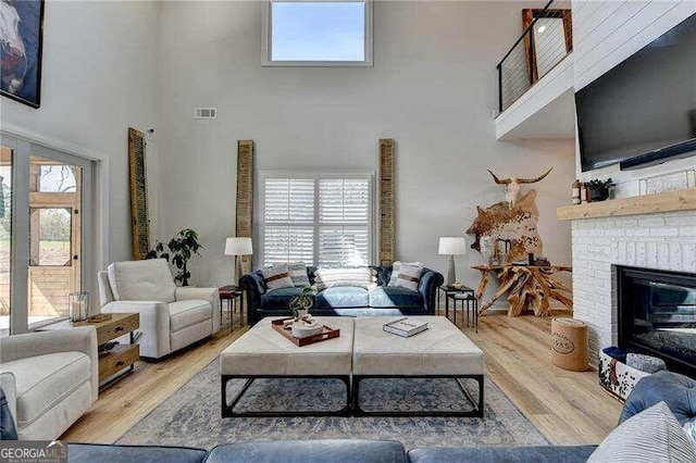 living room featuring a brick fireplace, a towering ceiling, a healthy amount of sunlight, and light wood-type flooring