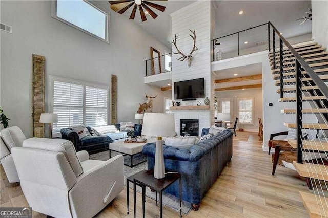 living room featuring plenty of natural light, light hardwood / wood-style floors, a towering ceiling, and a brick fireplace