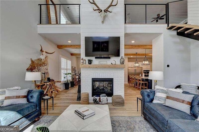 living room with a fireplace, beam ceiling, ceiling fan with notable chandelier, and hardwood / wood-style flooring