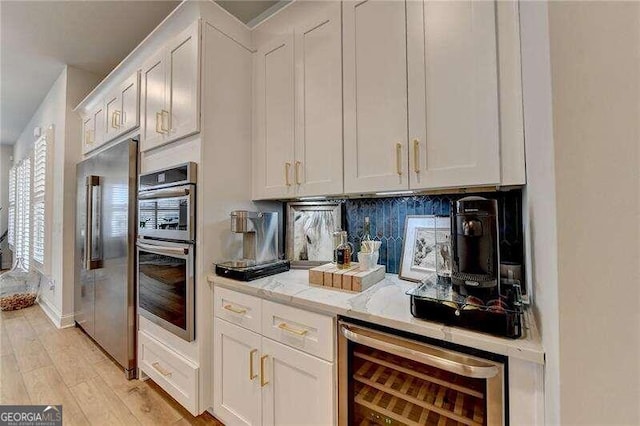 kitchen with decorative backsplash, appliances with stainless steel finishes, light stone counters, beverage cooler, and white cabinets