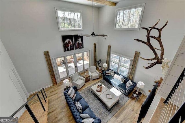 living room with ceiling fan, beam ceiling, light wood-type flooring, and a high ceiling