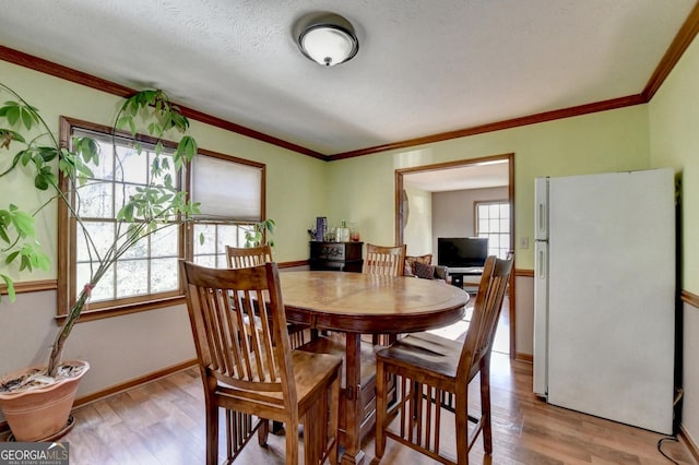 dining space with light hardwood / wood-style flooring, a textured ceiling, and ornamental molding