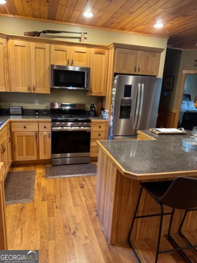 kitchen featuring stainless steel appliances, wooden ceiling, a breakfast bar area, light hardwood / wood-style flooring, and ornamental molding