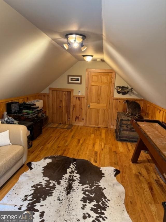 additional living space with wooden walls, vaulted ceiling, and light hardwood / wood-style flooring