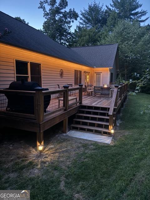 back house at dusk featuring a lawn and a deck