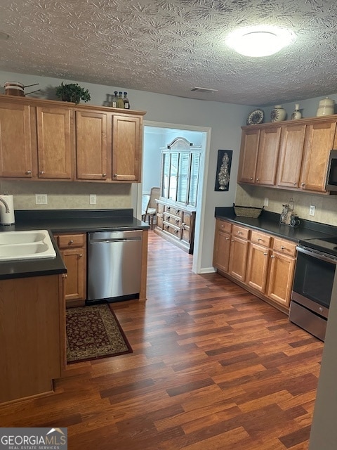 kitchen with appliances with stainless steel finishes, sink, dark hardwood / wood-style floors, and a textured ceiling