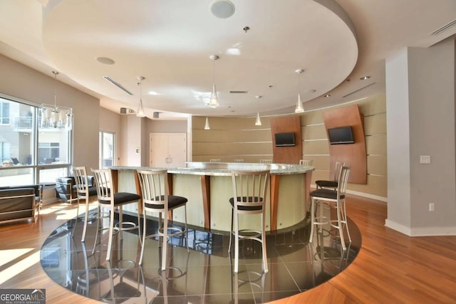 bar with light stone countertops, hanging light fixtures, and dark hardwood / wood-style floors