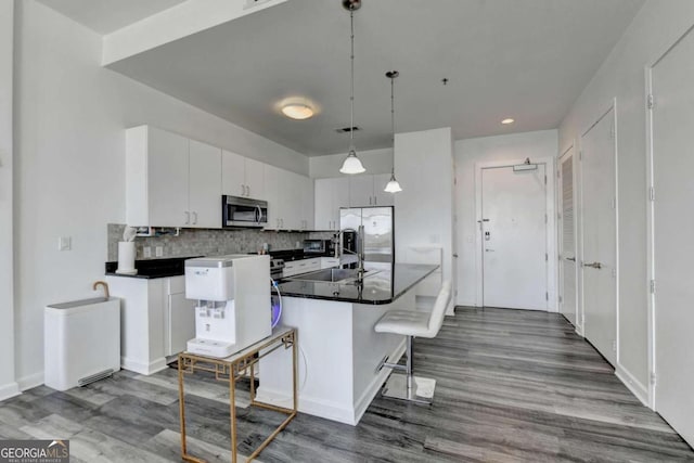 kitchen featuring dark hardwood / wood-style flooring, a breakfast bar, stainless steel appliances, hanging light fixtures, and white cabinets