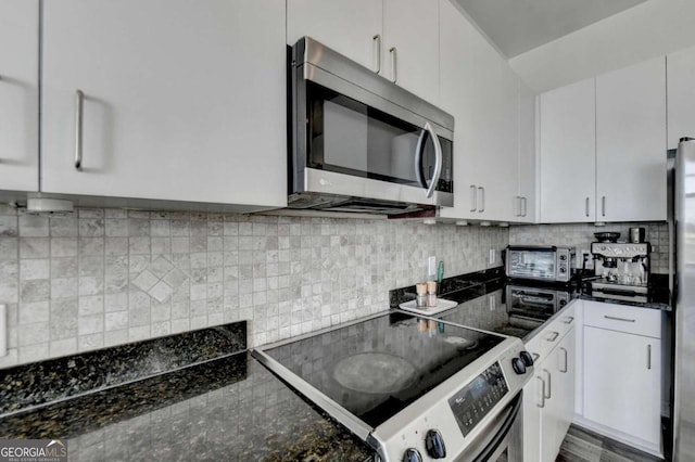 kitchen with dark stone countertops, white cabinets, backsplash, and electric range oven