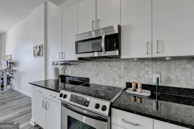 kitchen featuring stainless steel appliances, dark stone counters, light hardwood / wood-style floors, and white cabinetry