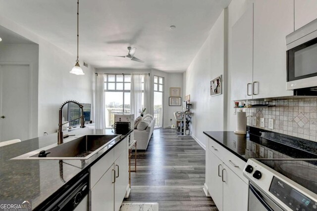 kitchen with stainless steel appliances, white cabinets, dark stone countertops, sink, and pendant lighting