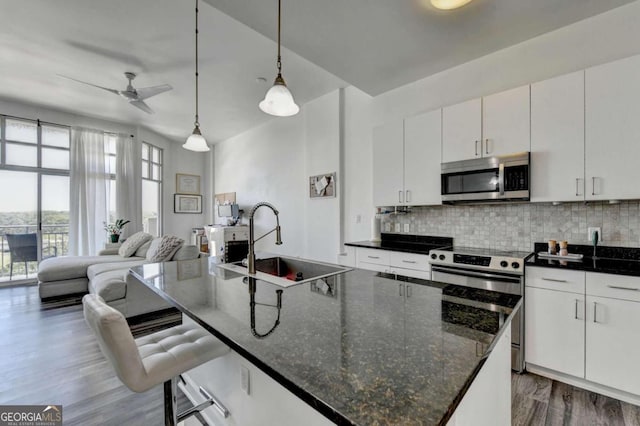 kitchen featuring a kitchen island with sink, stainless steel appliances, white cabinets, sink, and pendant lighting