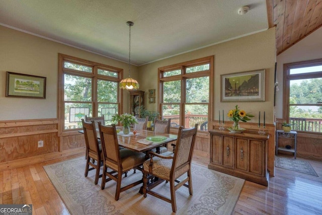 dining area featuring ornamental molding, wood walls, light hardwood / wood-style floors, and a textured ceiling