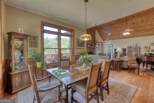 dining room featuring a stone fireplace, light hardwood / wood-style flooring, vaulted ceiling, and a wealth of natural light