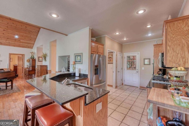 kitchen with dark stone countertops, vaulted ceiling, sink, stainless steel fridge with ice dispenser, and light tile patterned floors