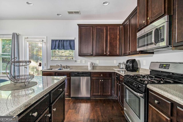 kitchen with light stone counters, dark brown cabinetry, dark wood-type flooring, sink, and appliances with stainless steel finishes