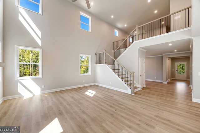 unfurnished living room featuring a towering ceiling, light hardwood / wood-style flooring, and ceiling fan