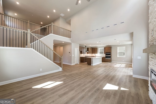 unfurnished living room featuring a towering ceiling, light hardwood / wood-style floors, sink, and a stone fireplace