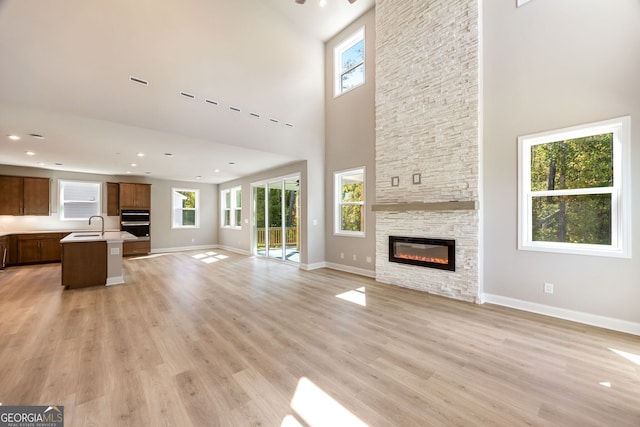 unfurnished living room with a towering ceiling, plenty of natural light, light wood-type flooring, and a stone fireplace