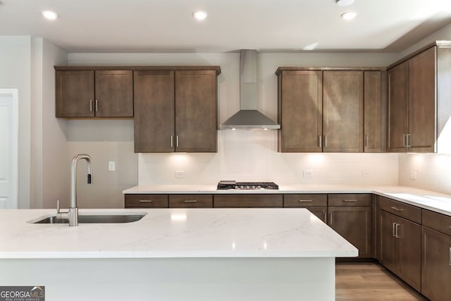 kitchen featuring light stone counters, wall chimney exhaust hood, sink, stainless steel gas cooktop, and light hardwood / wood-style flooring