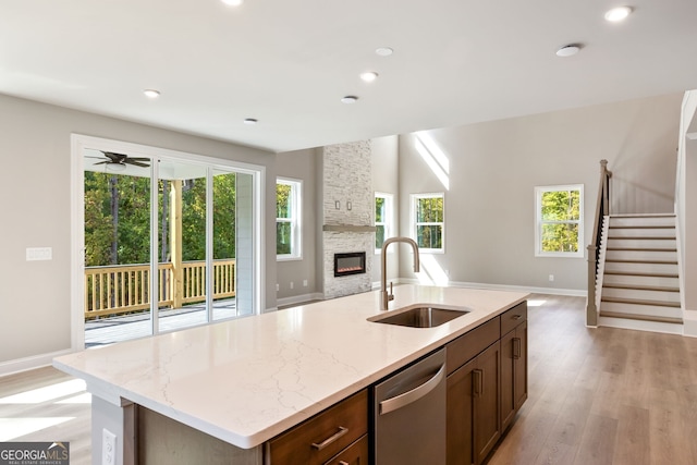 kitchen featuring a kitchen island with sink, sink, a fireplace, light hardwood / wood-style flooring, and dishwasher