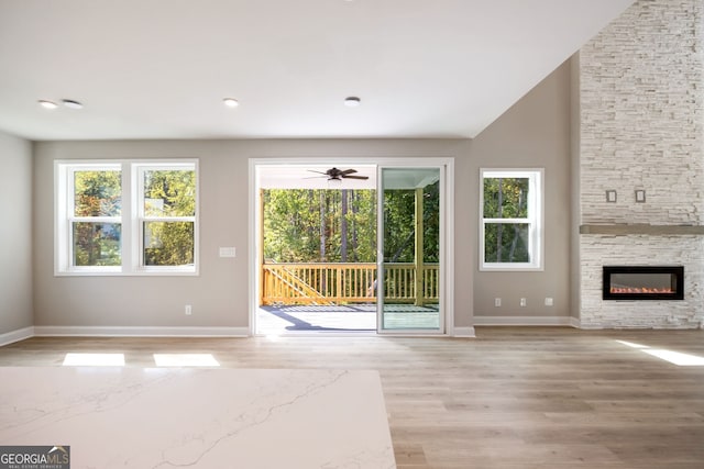 unfurnished living room featuring a fireplace, light hardwood / wood-style floors, vaulted ceiling, and a healthy amount of sunlight