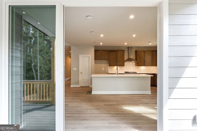 kitchen with sink, light hardwood / wood-style floors, wall chimney range hood, and gas cooktop