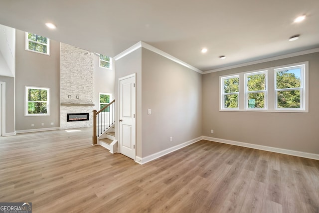 unfurnished living room with crown molding, a wealth of natural light, a stone fireplace, and light hardwood / wood-style flooring