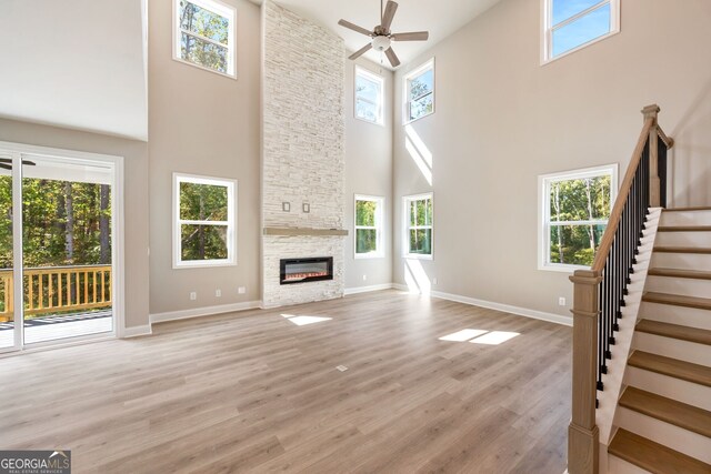 unfurnished living room featuring ceiling fan, a stone fireplace, light hardwood / wood-style floors, and a high ceiling