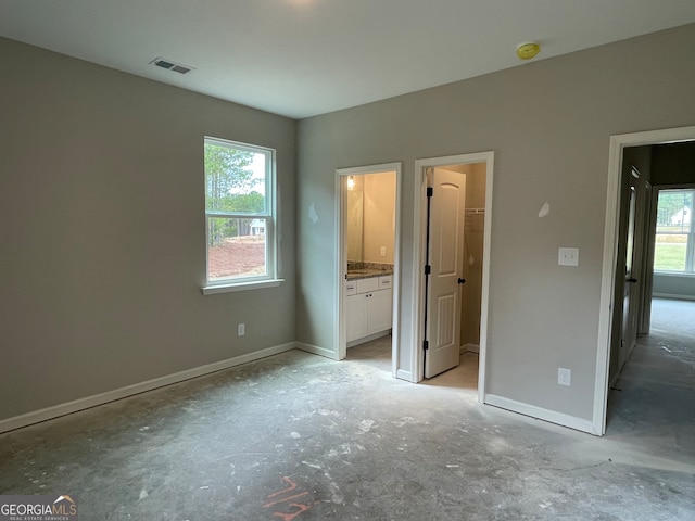 unfurnished bedroom featuring ensuite bathroom, multiple windows, and a spacious closet