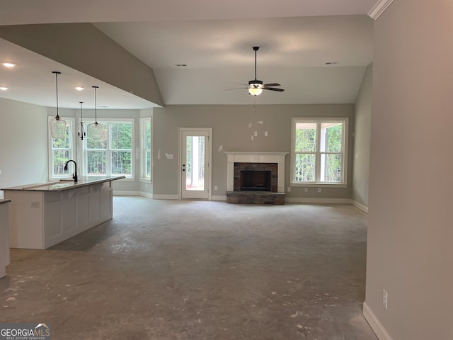 unfurnished living room with ceiling fan, vaulted ceiling, sink, and a stone fireplace