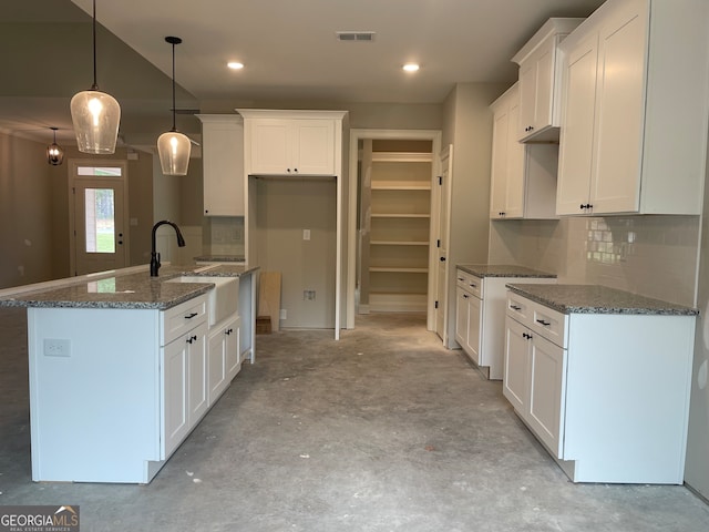 kitchen with a center island with sink, pendant lighting, dark stone counters, and white cabinetry