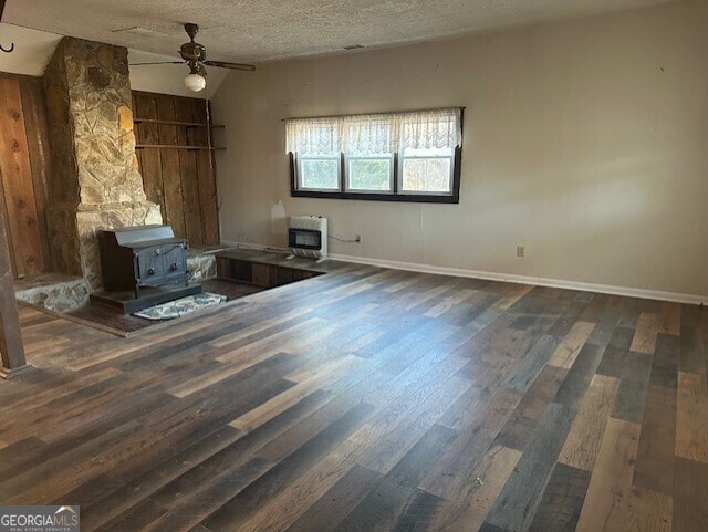 unfurnished living room with a wood stove, ceiling fan, dark wood-type flooring, heating unit, and a textured ceiling