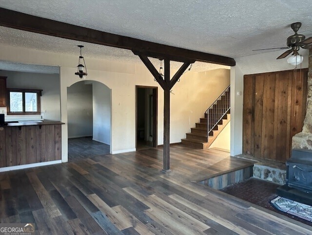 unfurnished living room with beam ceiling, wood walls, dark hardwood / wood-style floors, and a textured ceiling