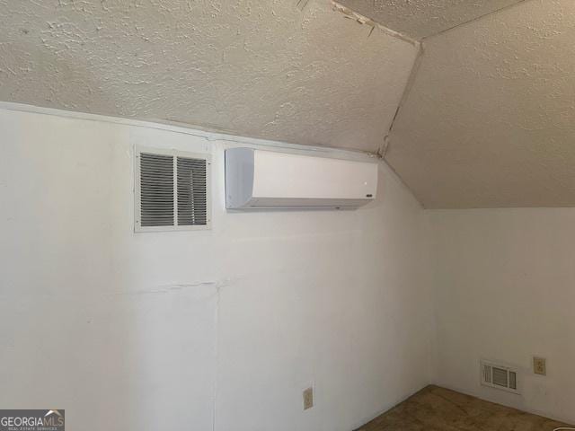 bonus room with a textured ceiling, a wall unit AC, and vaulted ceiling