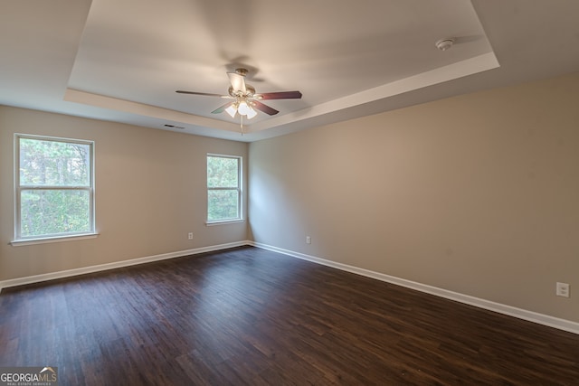 empty room with a raised ceiling, ceiling fan, and dark hardwood / wood-style floors