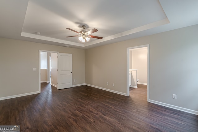 unfurnished bedroom featuring ceiling fan, ensuite bathroom, dark wood-type flooring, and a tray ceiling