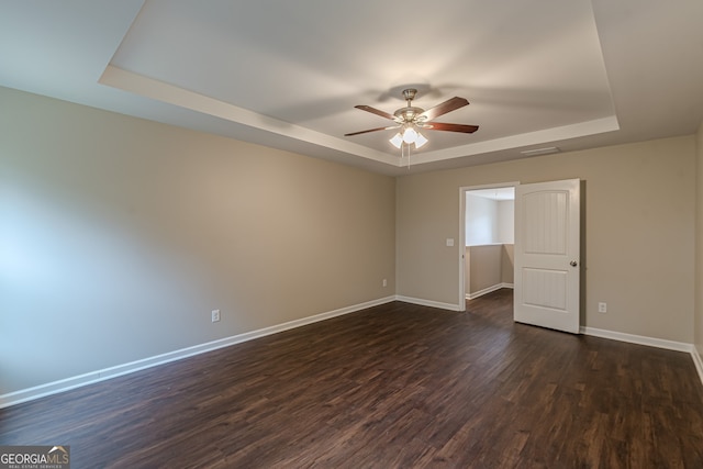 empty room with dark hardwood / wood-style floors, a raised ceiling, and ceiling fan