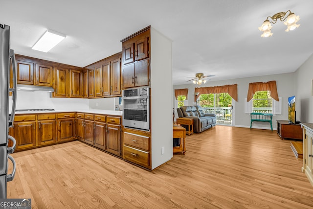 kitchen with ceiling fan, cooktop, stainless steel oven, and light wood-type flooring