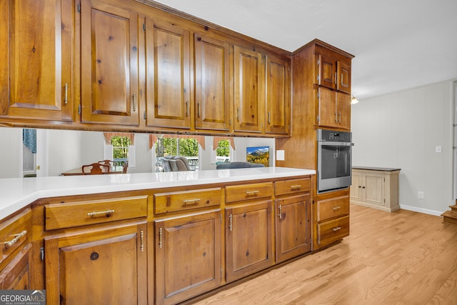 kitchen featuring wood walls, stainless steel oven, light hardwood / wood-style flooring, and kitchen peninsula