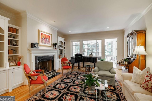 living room with crown molding, built in features, a fireplace, and light hardwood / wood-style floors