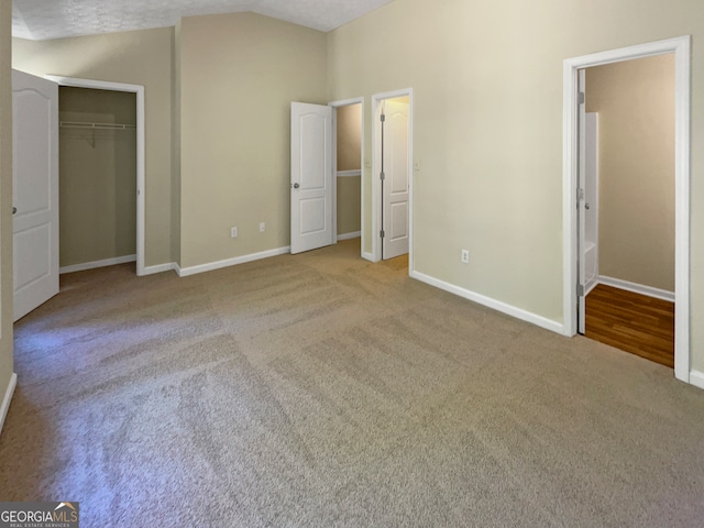 unfurnished bedroom featuring a closet, vaulted ceiling, a textured ceiling, and light carpet