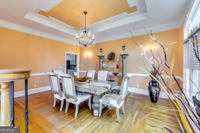 dining area with an inviting chandelier, a tray ceiling, crown molding, and light hardwood / wood-style floors