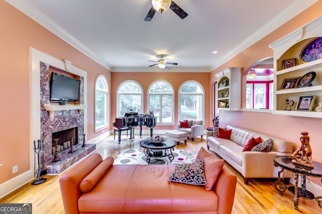 living room featuring ceiling fan, light wood-type flooring, a premium fireplace, and crown molding